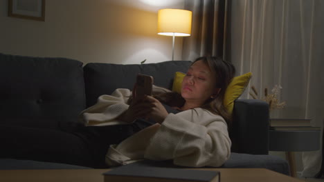 Woman-Spending-Evening-At-Home-Lying-On-Sofa-With-Mobile-Phone-Scrolling-Through-Internet-Or-Social-Media-1